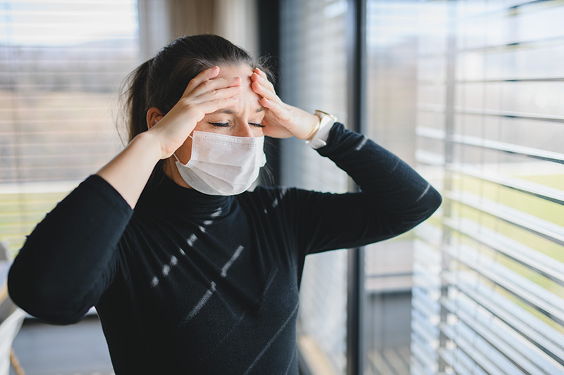 Woman with headache and face masks indoors at home, Corona virus quarentine