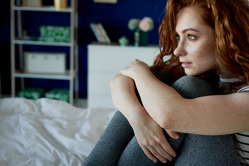 Redhead thoughtful woman in her bed thinking while holding her legs against her body