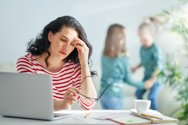 woman working on a laptop holding glasses in her hands and touching her head with a painful headache