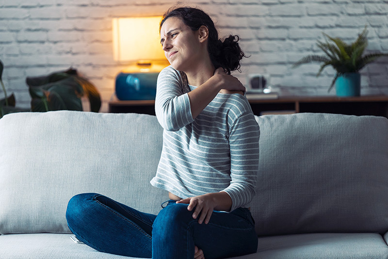 Young woman with back pain sitting on the sofa in the living room at home