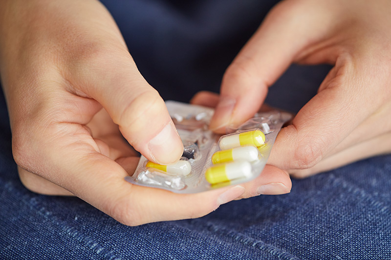 woman removing a pain killer pill from a plastic package for addiction