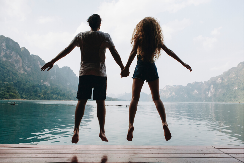 Man and woman holding hands and jumping off a dock into water